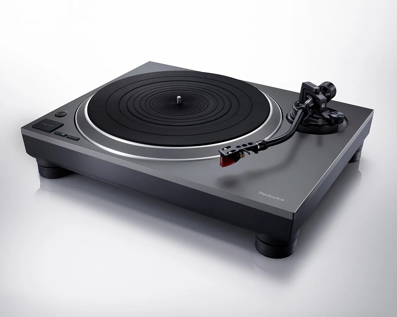 Gray and black Technics turntable with tonearm and cartridge on a white reflective surface.