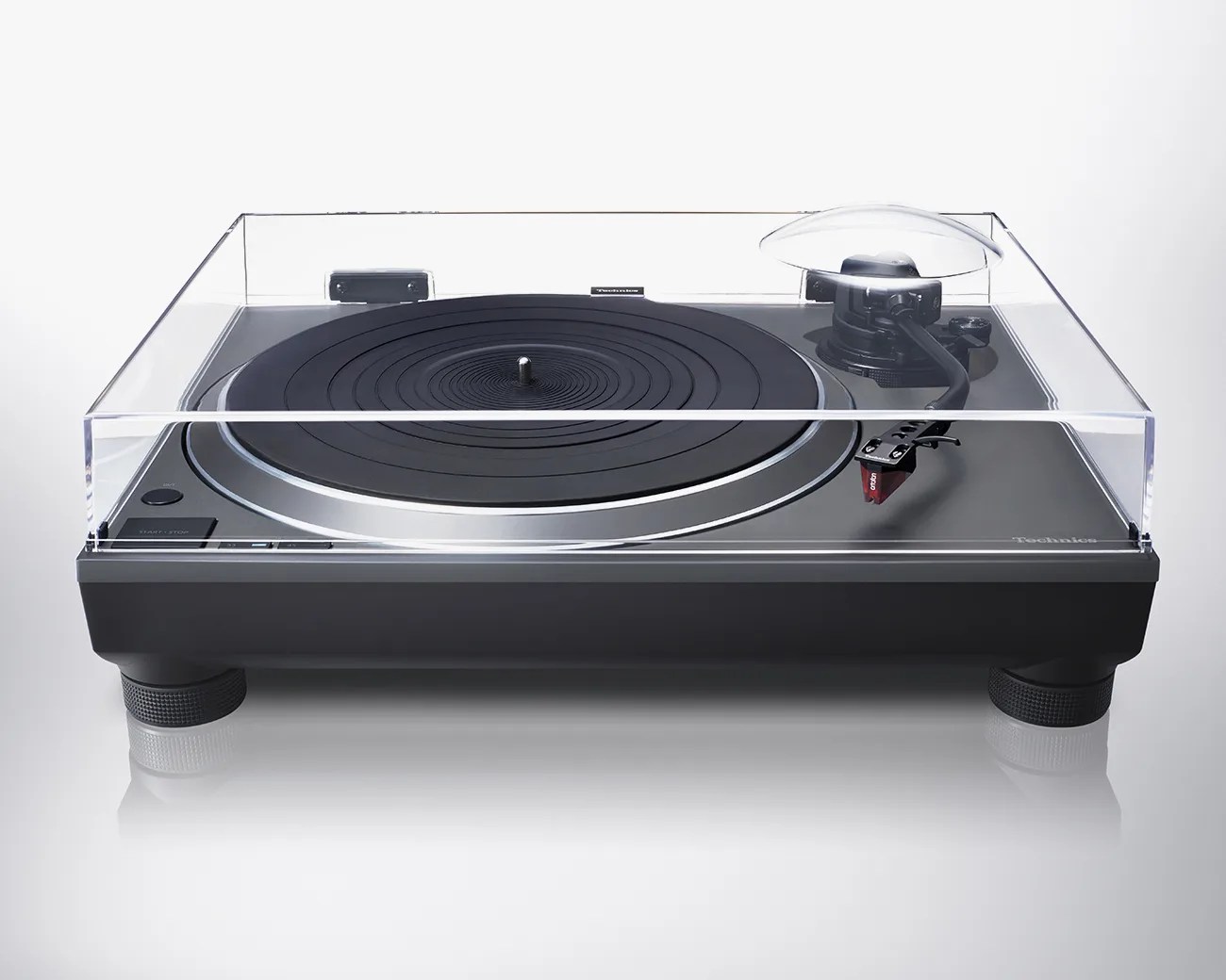 Black Technics turntable with transparent dust cover and red cartridge on a white background.