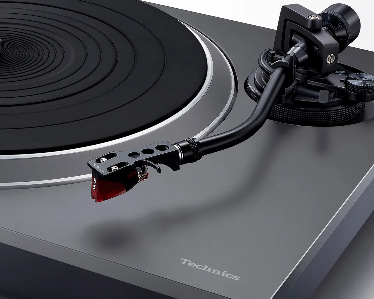 Close-up of a black and gray Technics turntable tonearm with a red Ortofon cartridge on a gray base.