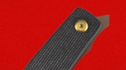 Black textured folding knife handle with a brass pivot screw and partially visible blade on a red background.