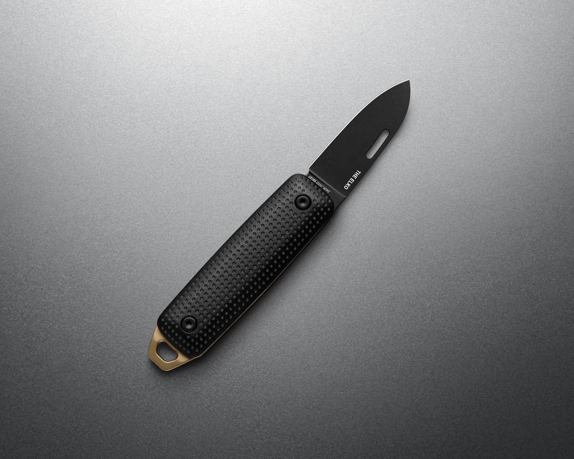 Black folding knife with textured handle and brass lanyard hole on a gray surface.