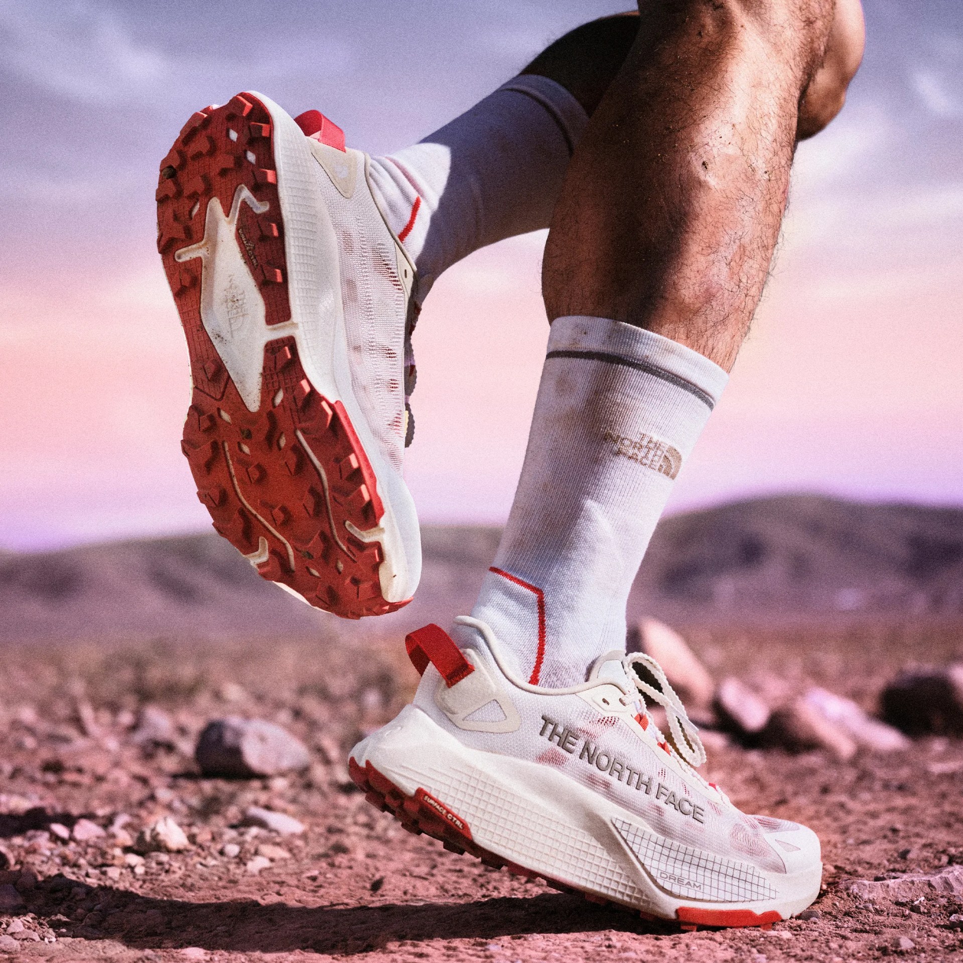 White and red The North Face trail running shoes worn with white socks on rocky terrain.