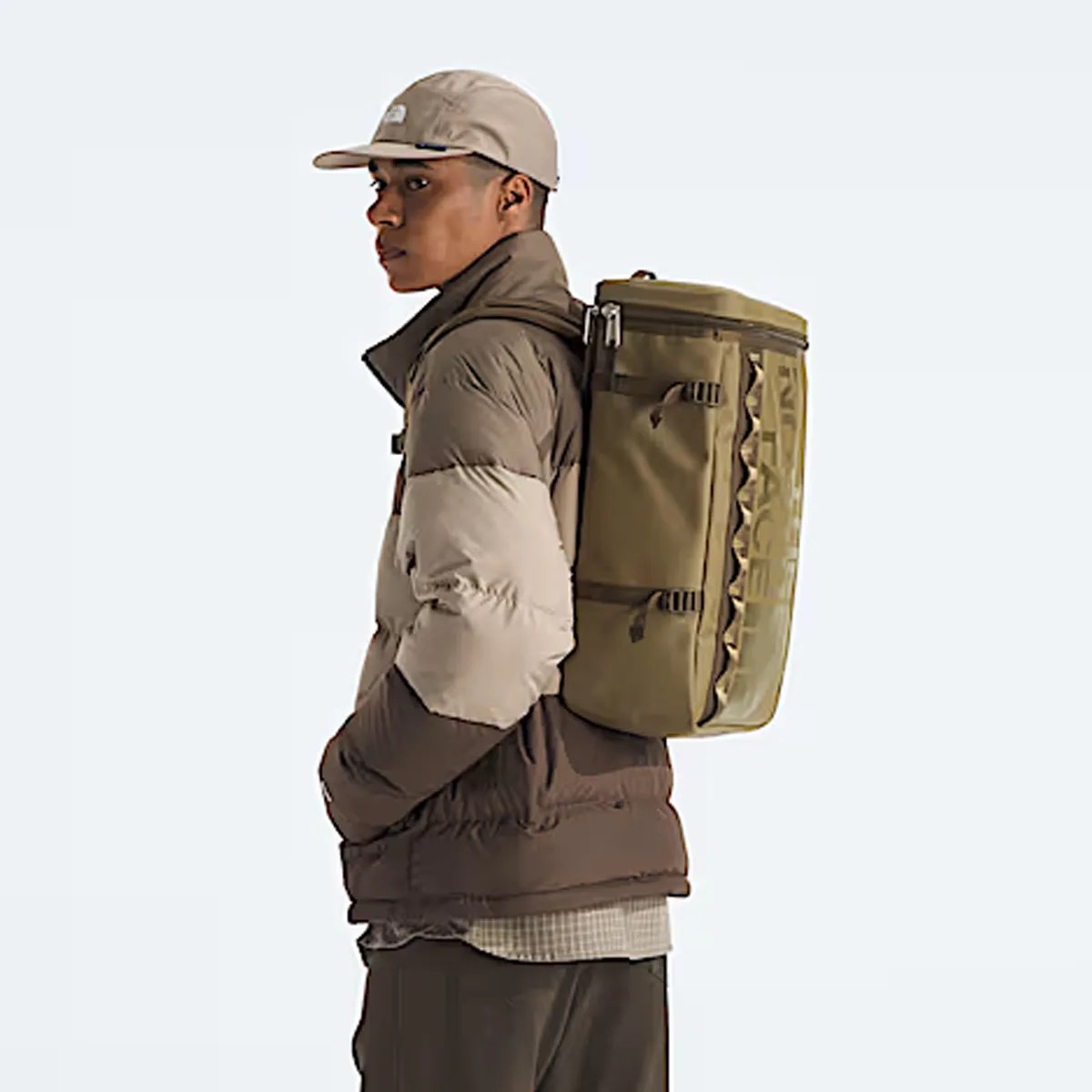 Person wearing a beige and brown puffer jacket and beige cap with an olive green rectangular backpack.