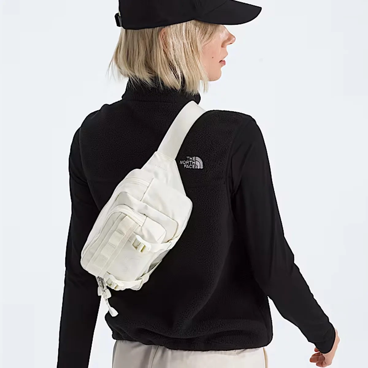 White crossbody bag with multiple zippered compartments worn over a black fleece vest.