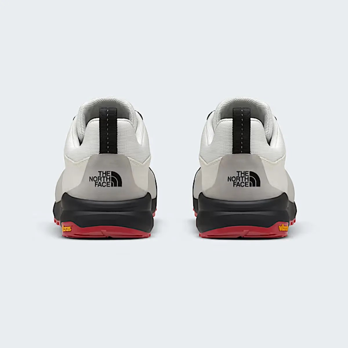 Pair of white and black The North Face sneakers with red soles shown from the back.