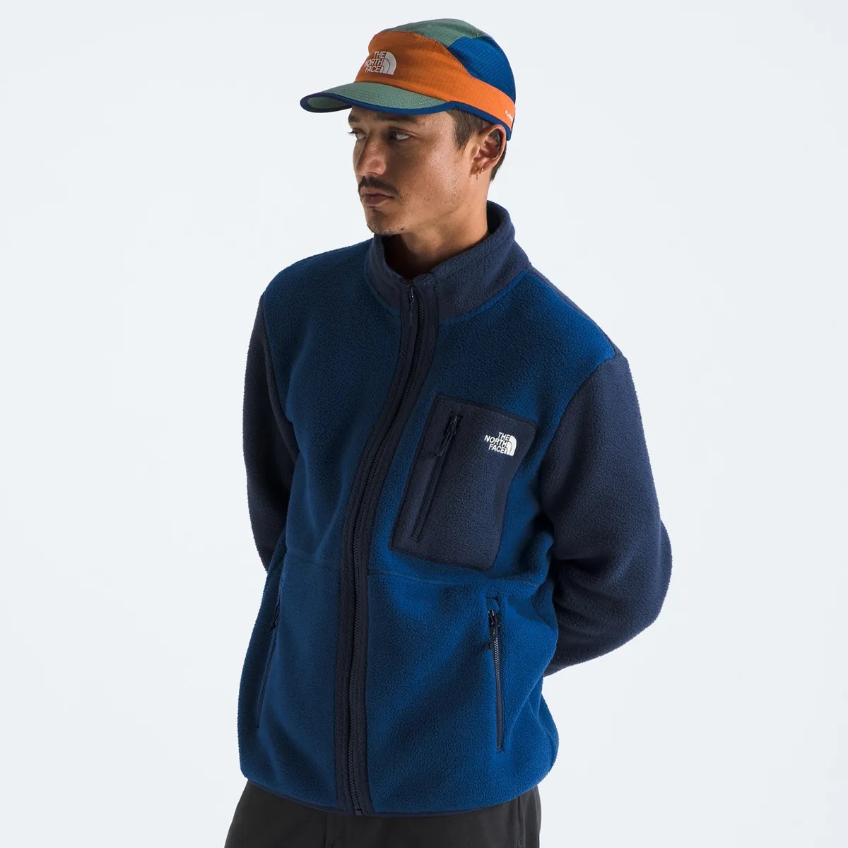 Man wearing a blue and navy fleece jacket with zippered pockets and a multicolor cap.