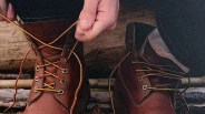 Person tying yellow and brown laces on brown leather boots.
