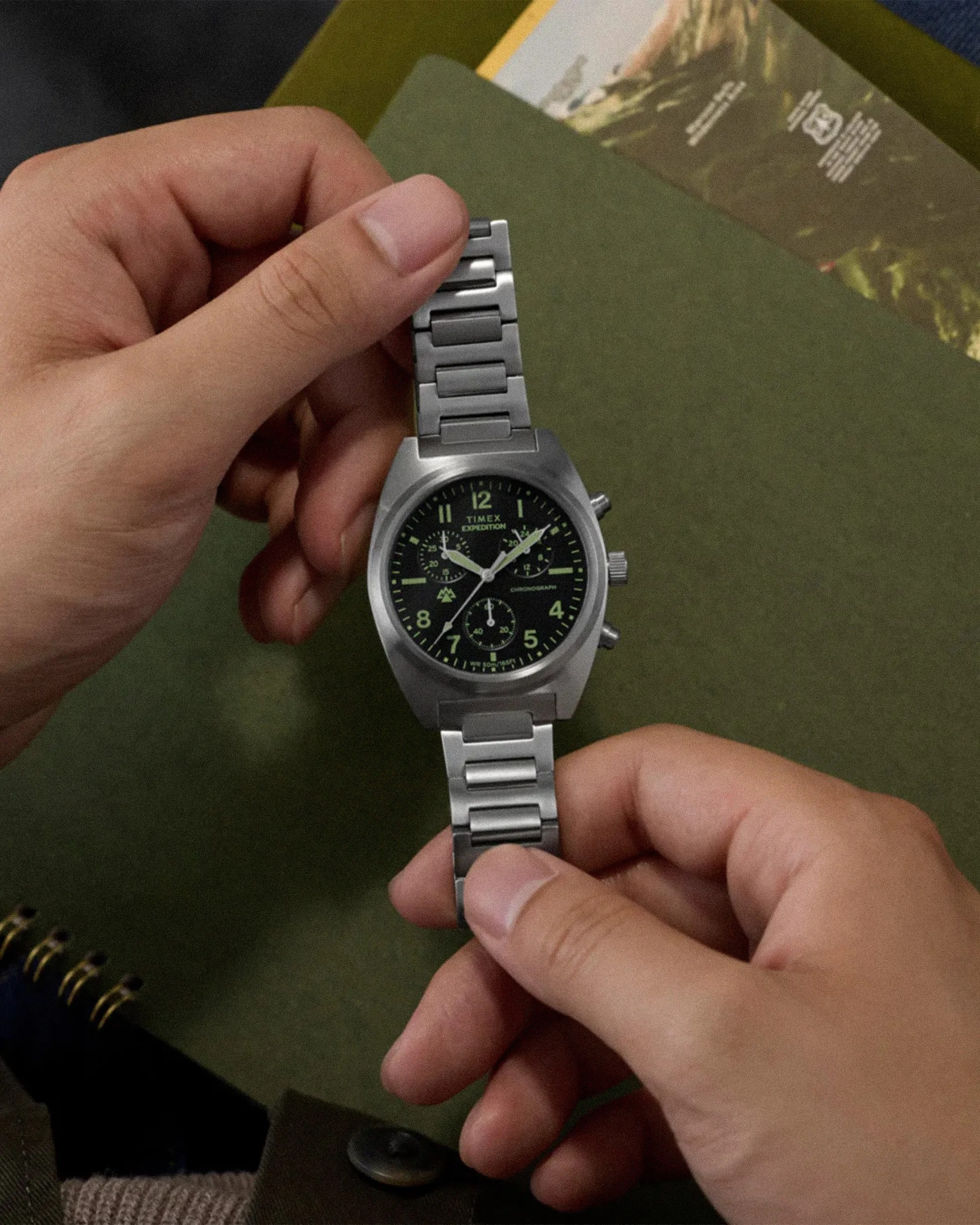 Silver Timex Expedition chronograph watch with black dial and metal link bracelet held in two hands.