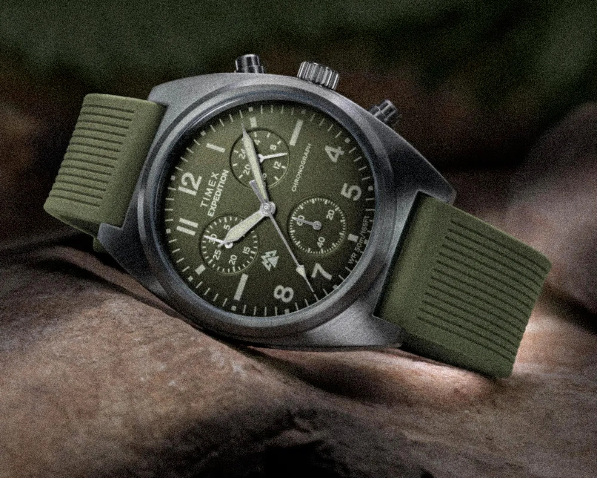 Timex Expedition chronograph watch with olive green dial and matching ribbed silicone strap on a rock surface.