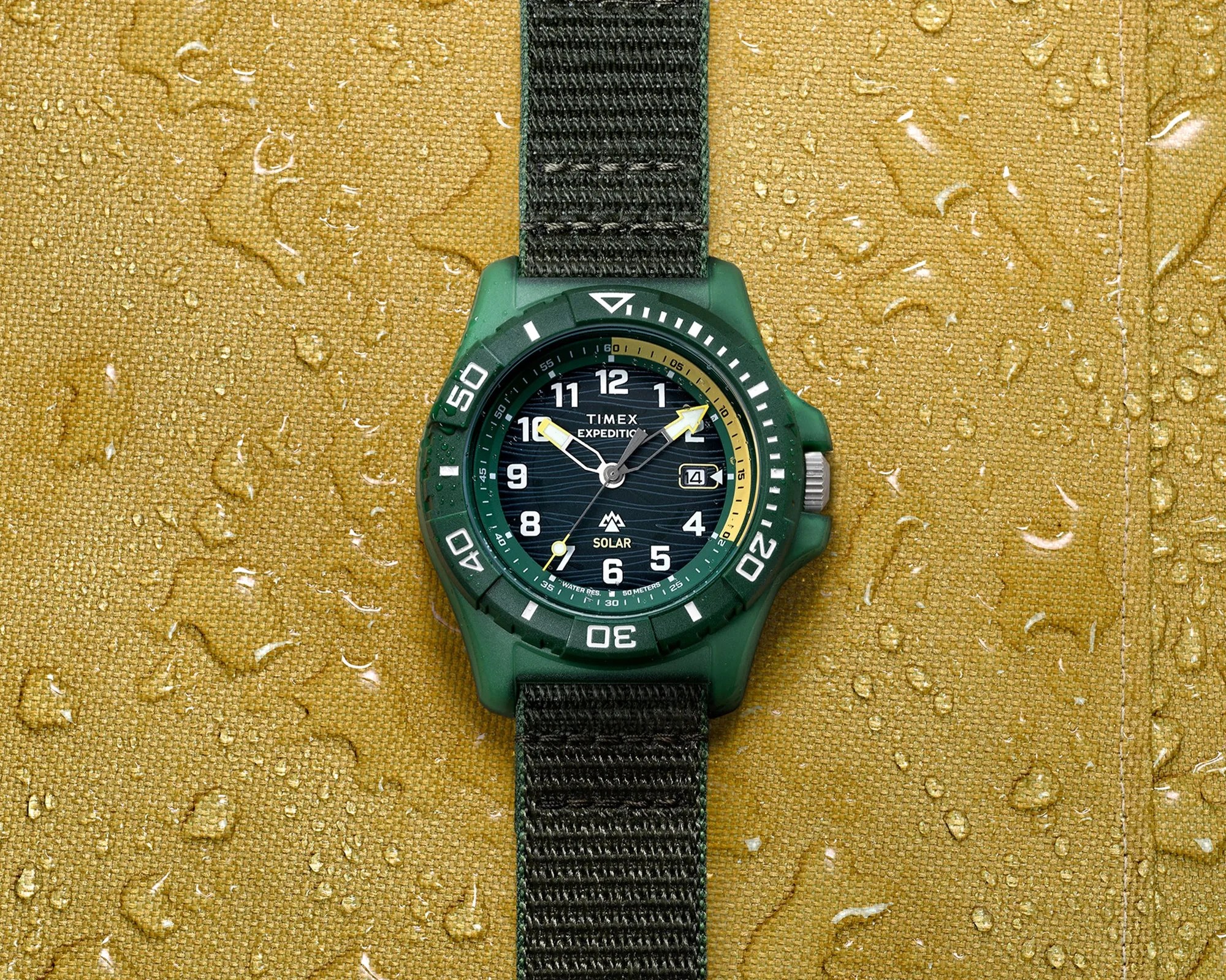 Green Timex Expedition solar watch with black fabric strap on wet yellow fabric.