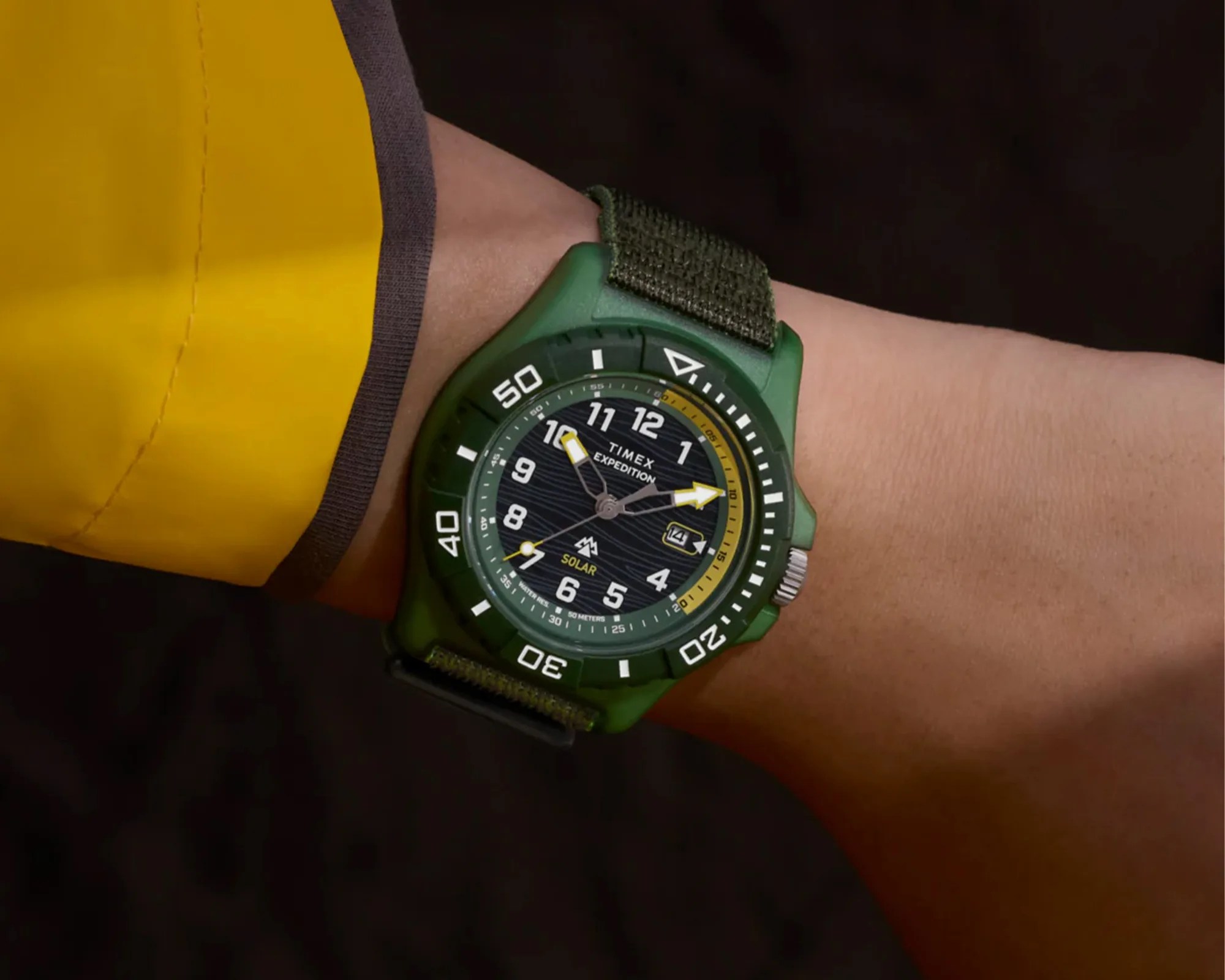Green Timex Expedition solar watch with black dial and yellow accents on a wrist.