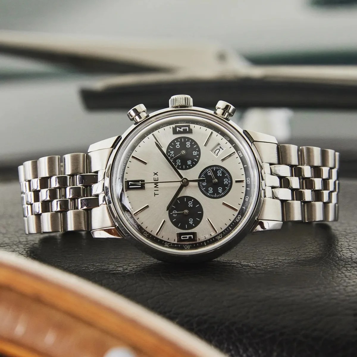 Silver Timex chronograph wristwatch with black subdials and a metal link bracelet on a black surface.