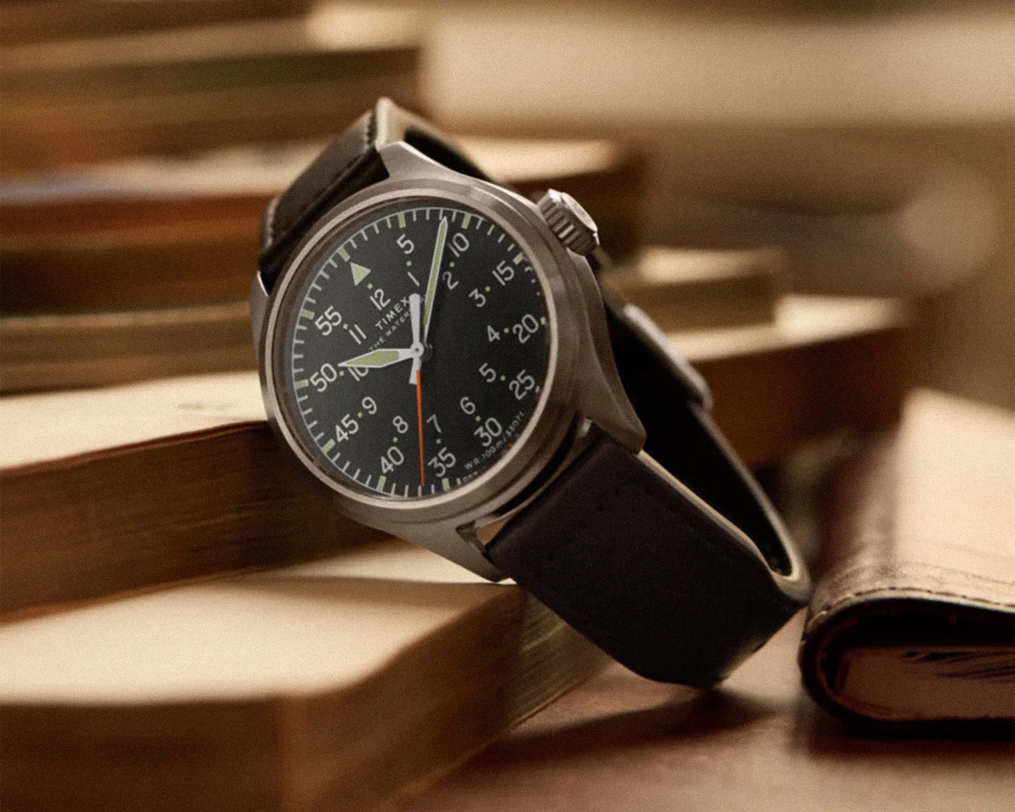 Timex wristwatch with black dial, white numerals, and black leather strap resting on stacked books.