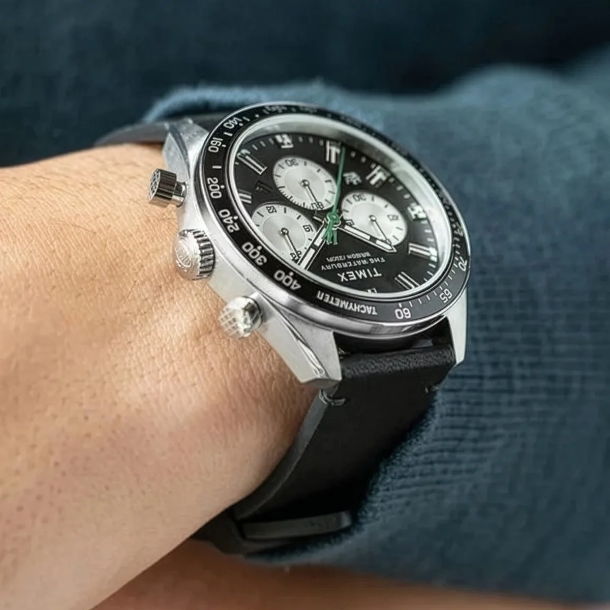Silver Timex chronograph watch with black dial, white subdials, and black leather strap on a wrist.