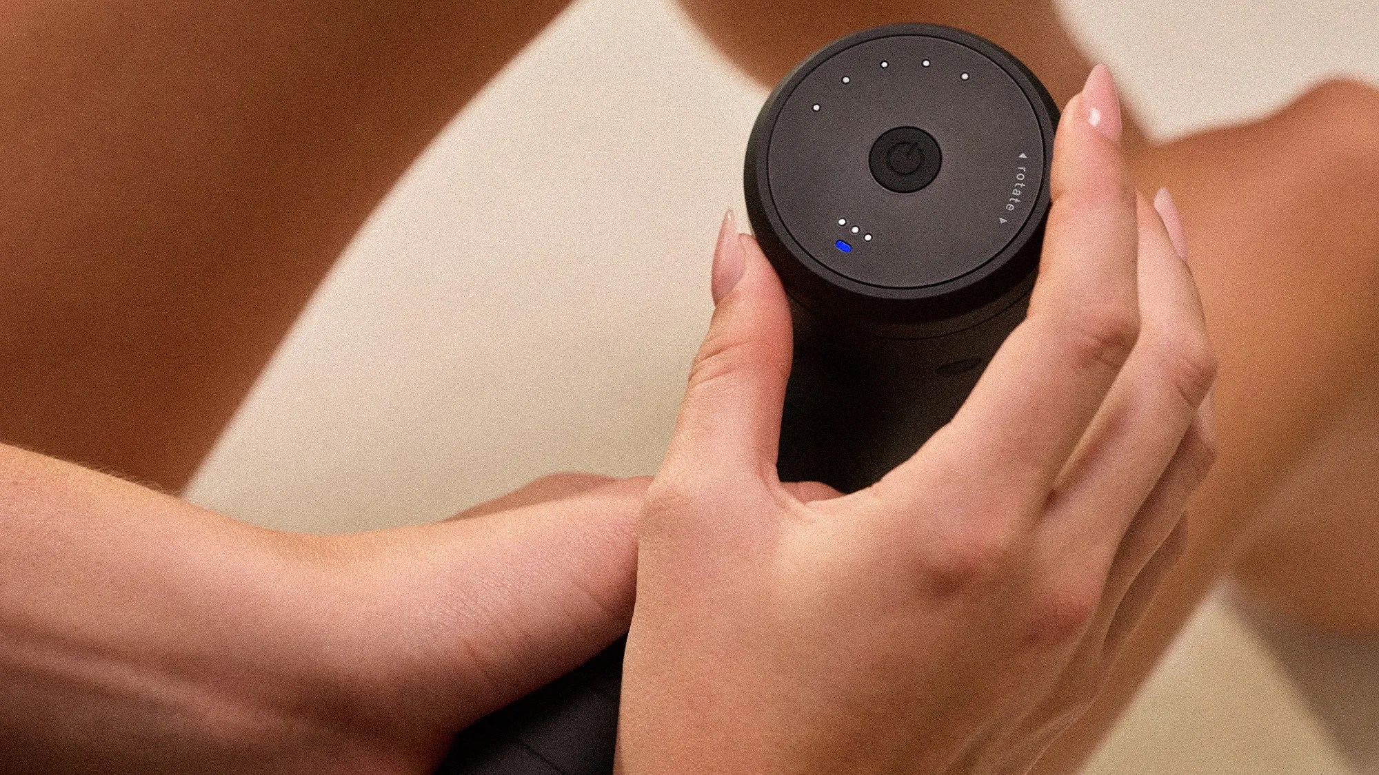 Black cylindrical electronic device with power button and LED indicators held in two hands.