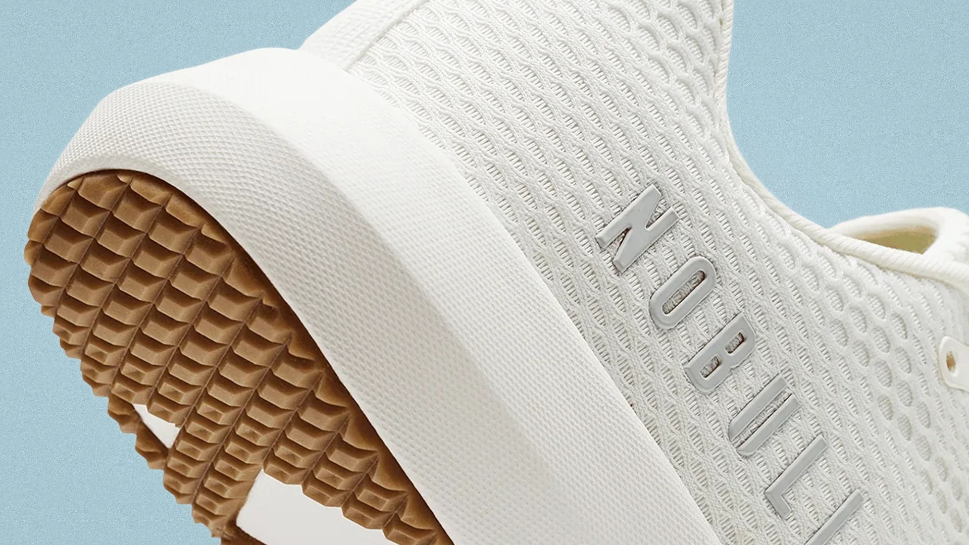 Close-up of a white sneaker with textured mesh upper, white midsole, and brown rubber outsole with "NOBULL" branding.