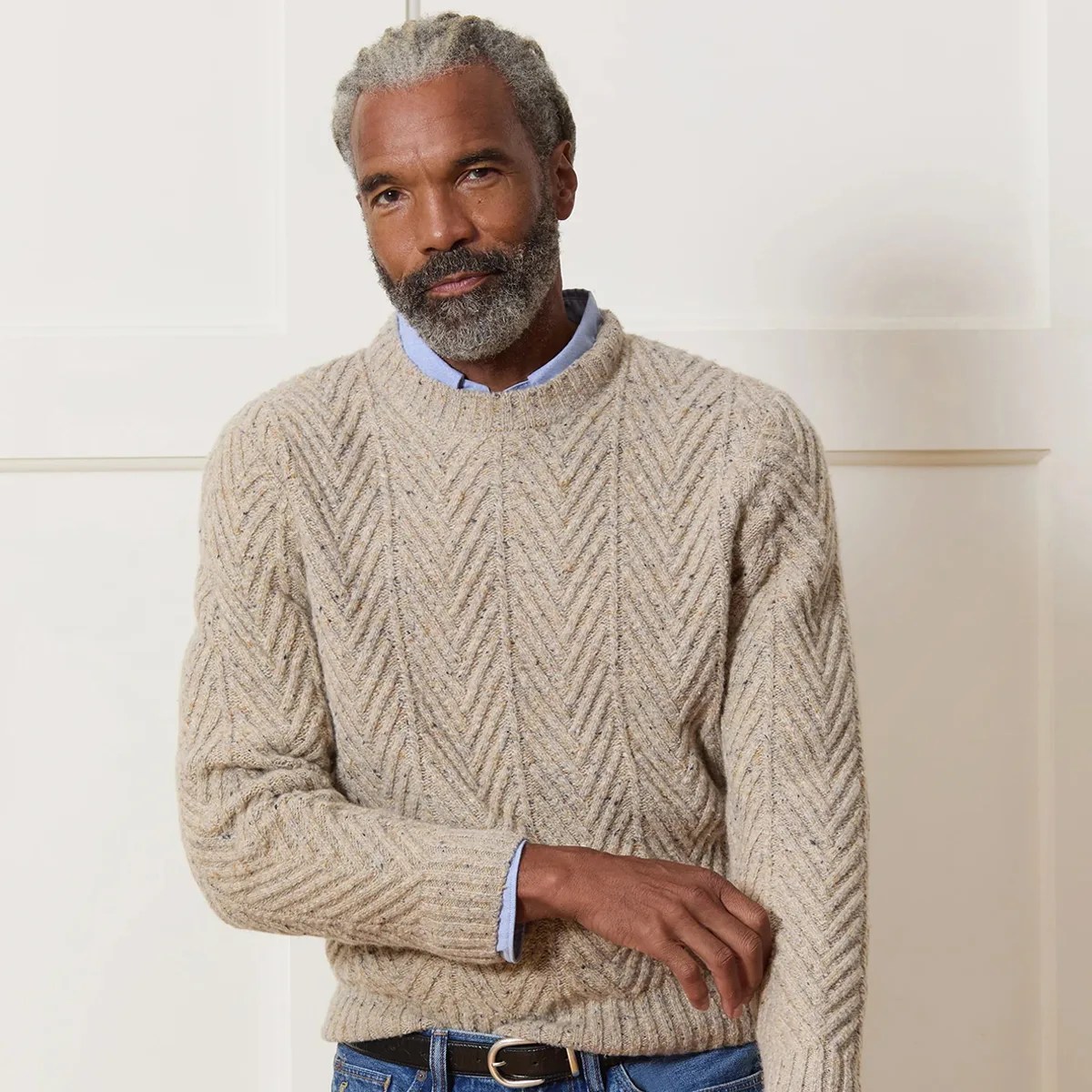 Beige cable-knit sweater with a chevron pattern worn over a light blue shirt.