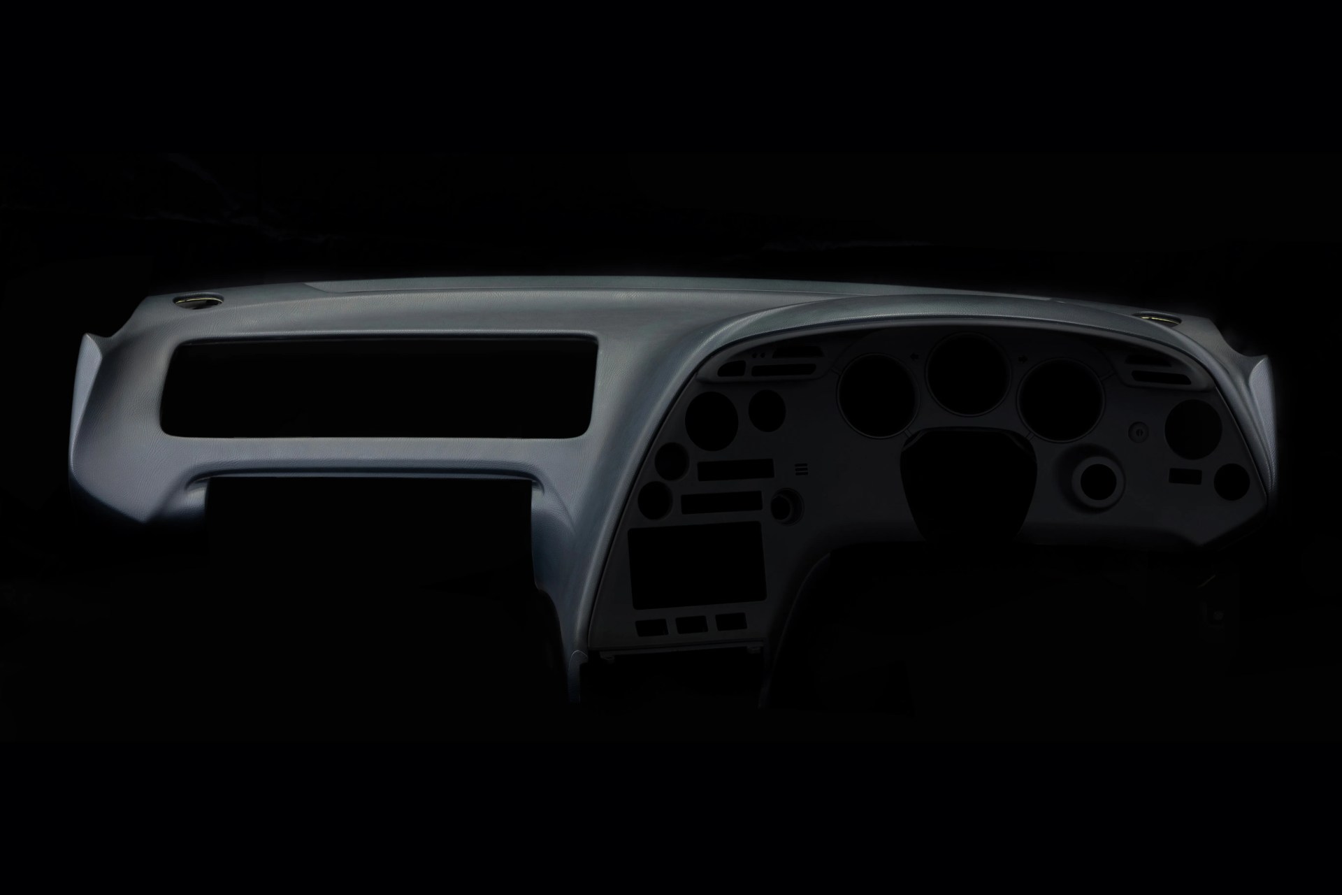 Gray car dashboard panel with multiple circular and rectangular cutouts for instruments and controls.