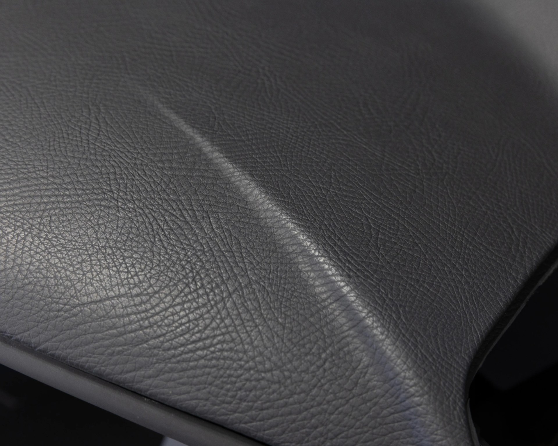 Close-up of black leather surface with a visible crease and textured grain.