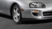 Front left side of a silver car showing the headlight, turn signal, and five-spoke alloy wheel with Bridgestone tire.