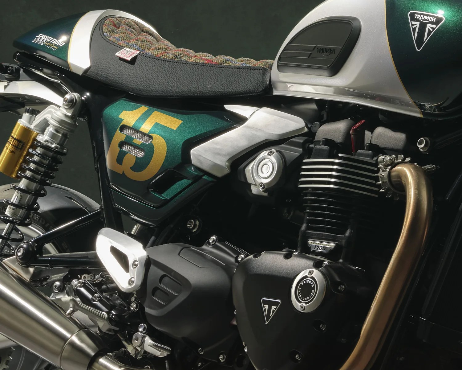 Close-up of a green and silver Triumph Speed Twin 1200 motorcycle engine and seat with gold "15" decal.