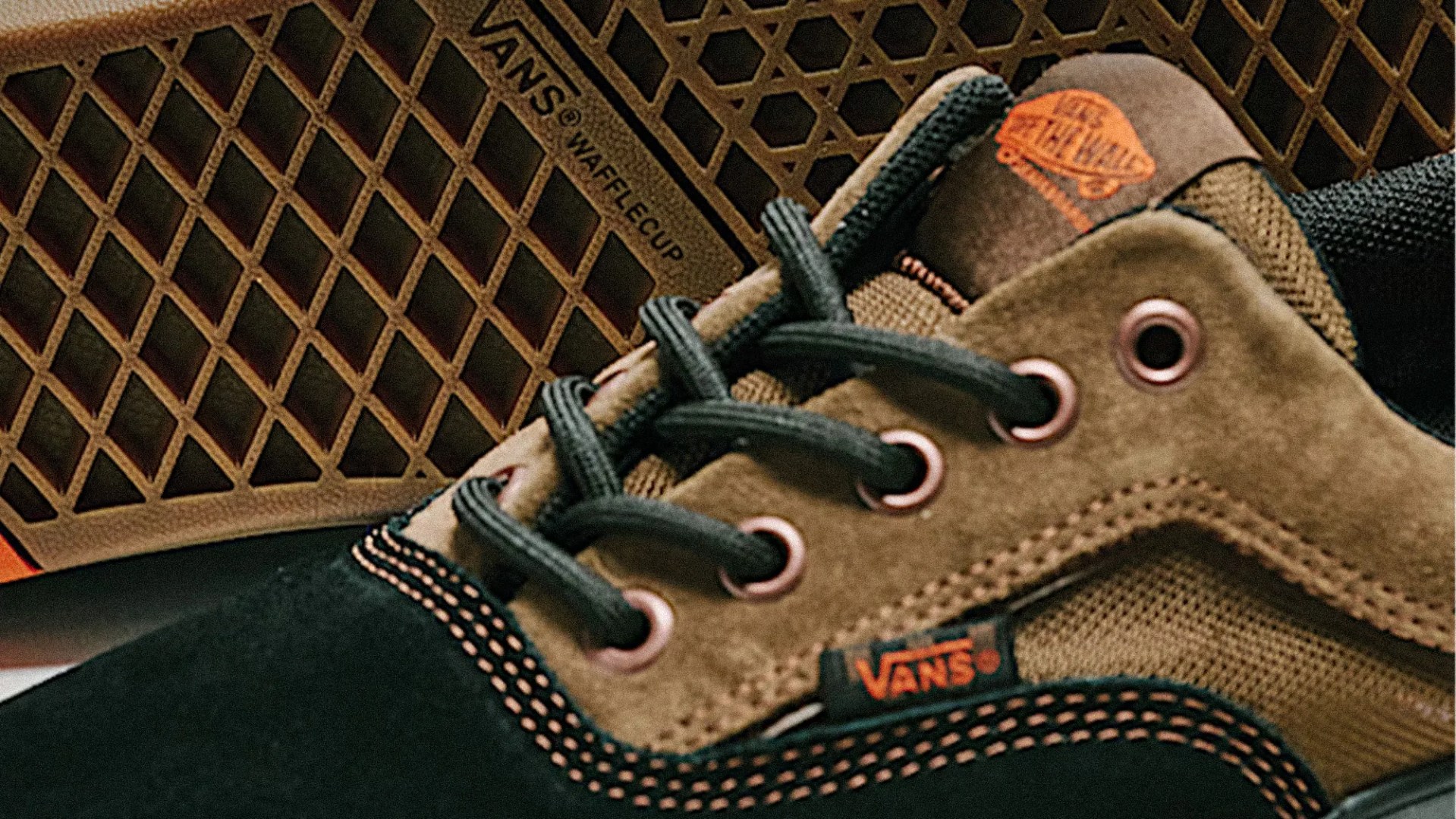 Close-up of a brown and black Vans sneaker with black laces and orange stitching, showing the Vans logo and waffle cup sole.