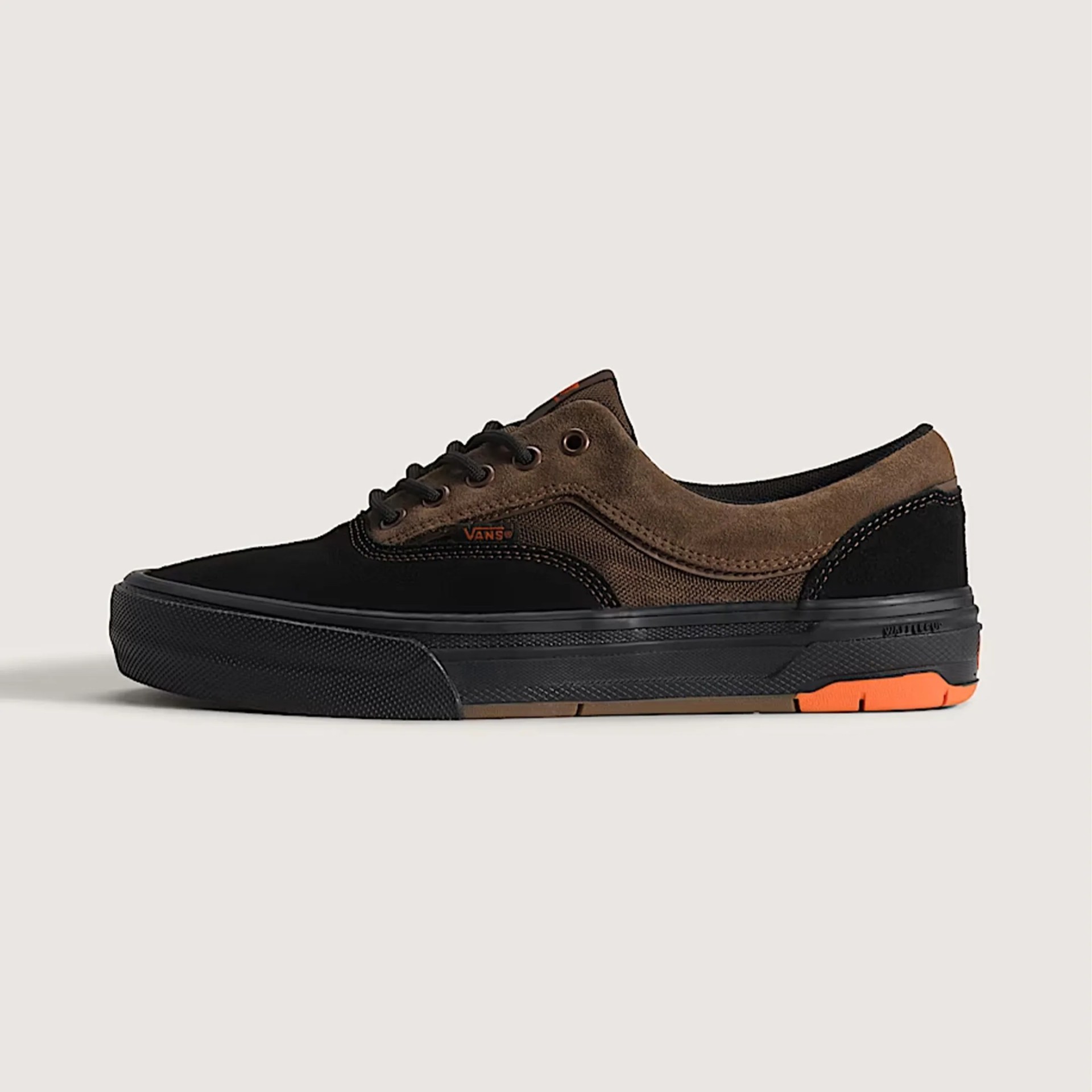 Low-top Vans sneaker in black and brown suede with black rubber sole and orange accents.