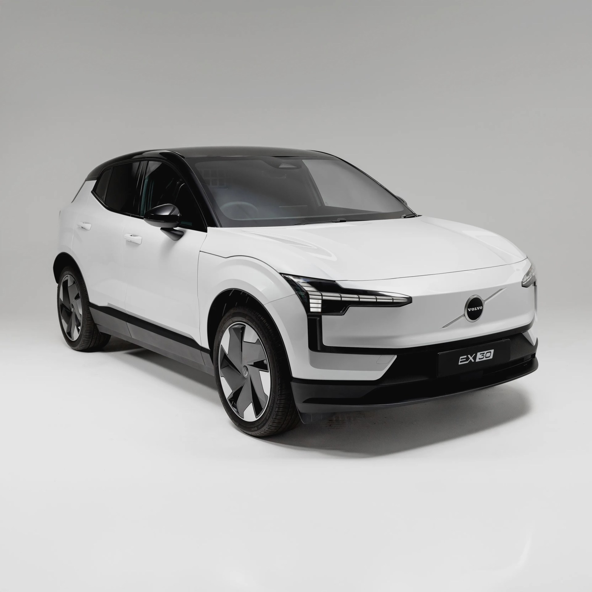 White Volvo EX30 electric SUV with black roof and modern angular headlights on a white studio background.