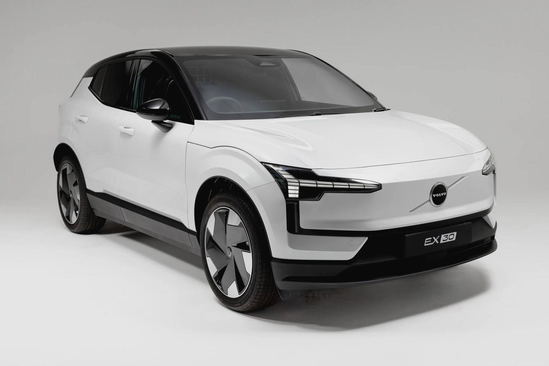 White Volvo EX30 electric SUV with black roof and modern angular headlights in a studio setting.