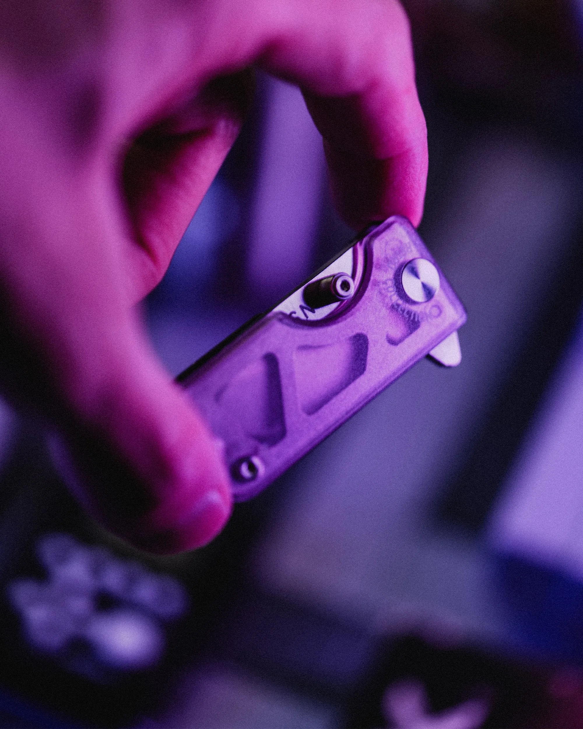 Hand holding a small purple metal multitool with a visible screw and a clip.