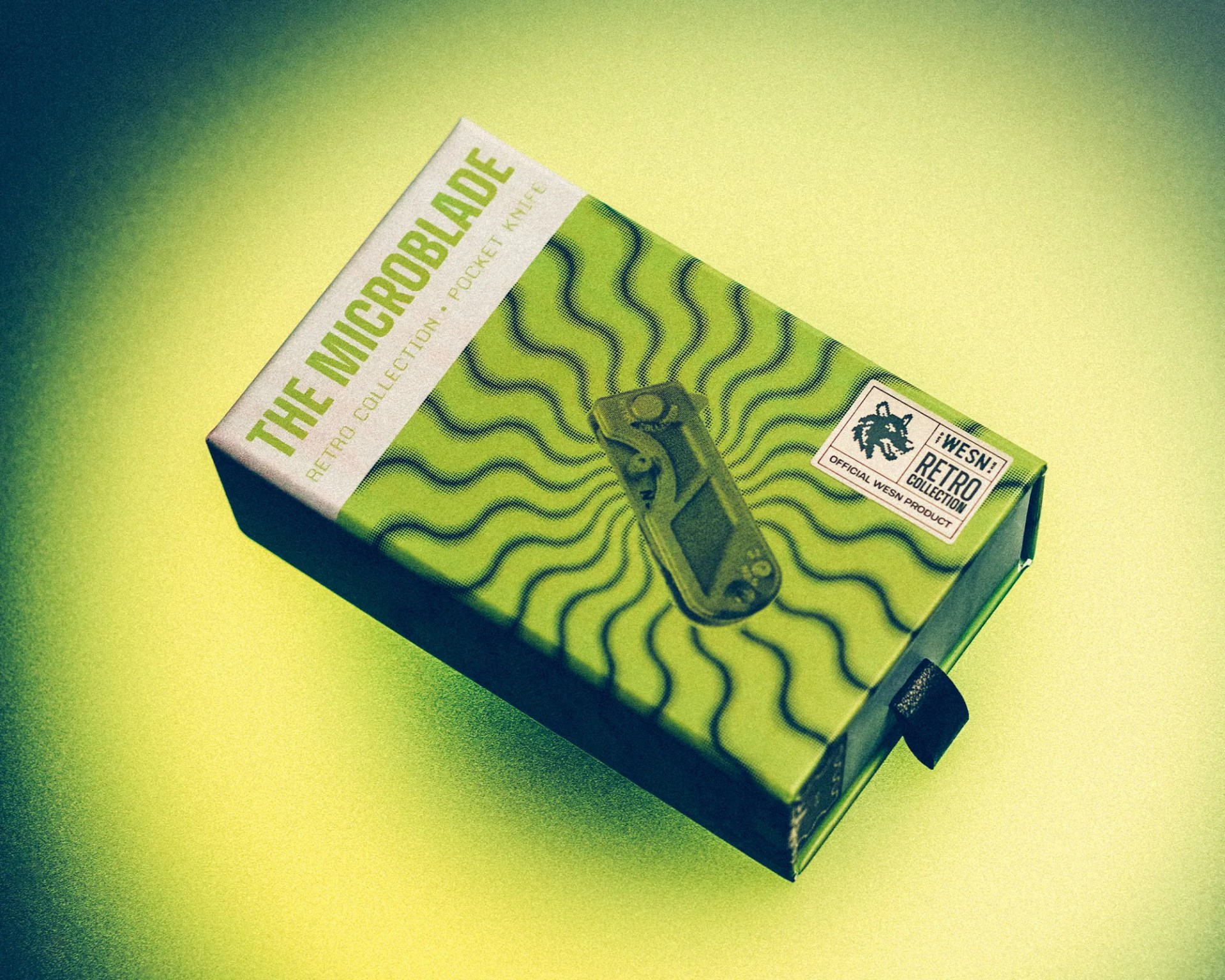 Green and white box labeled "The Microblade Retro Collection Pocket Knife" with wavy black lines and a small black pull tab.
