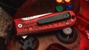 Red translucent folding knife with black clip resting on a red translucent gaming controller.