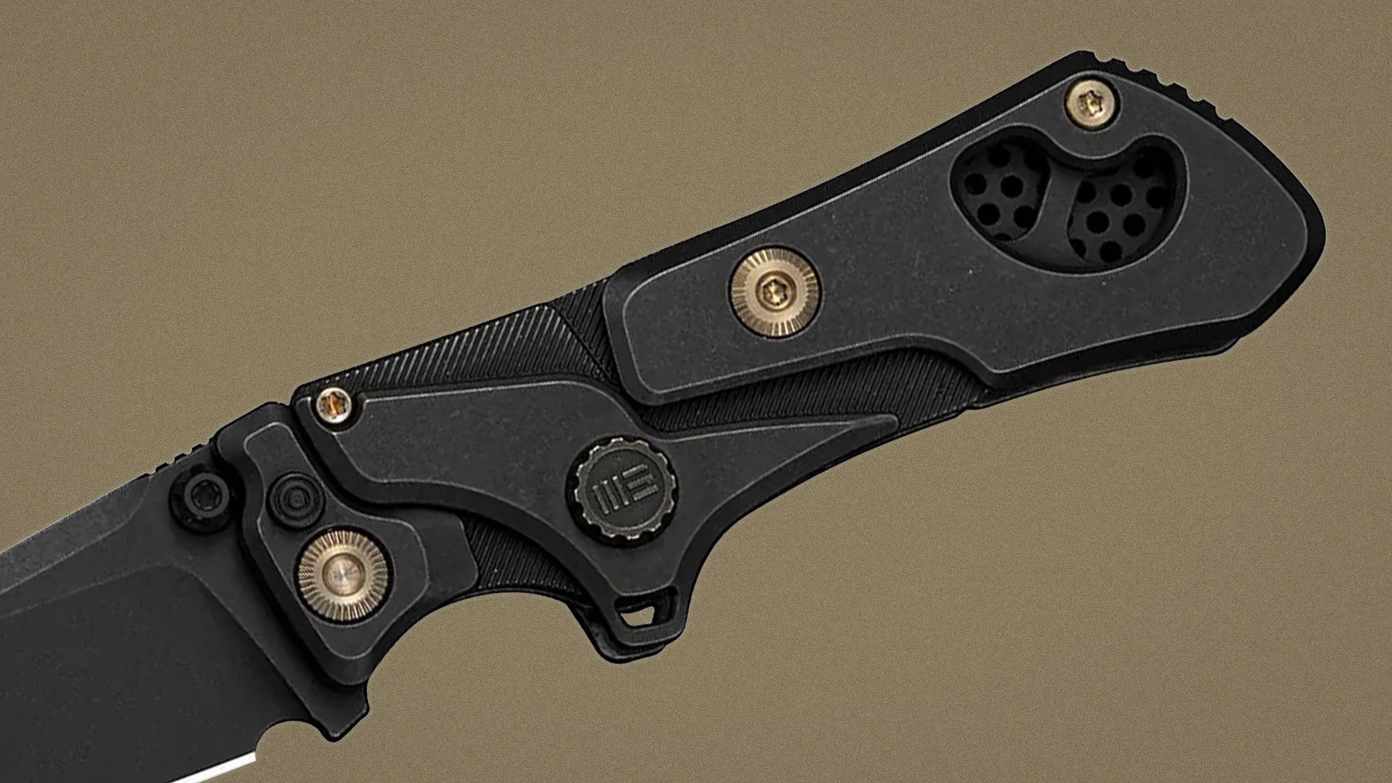 Black folding knife handle with textured grip, brass screws, and a circular black pivot with a logo.