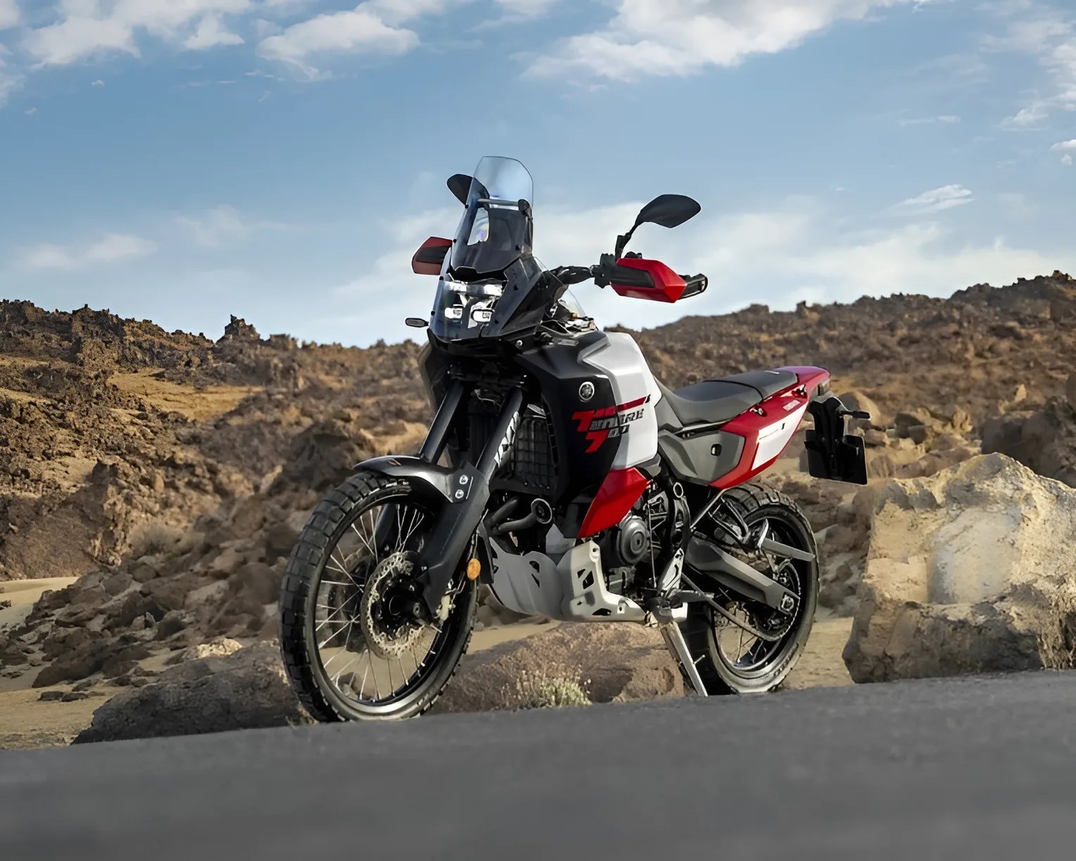 Black, white, and red adventure motorcycle with knobby tires parked on a road with rocky terrain in the background.