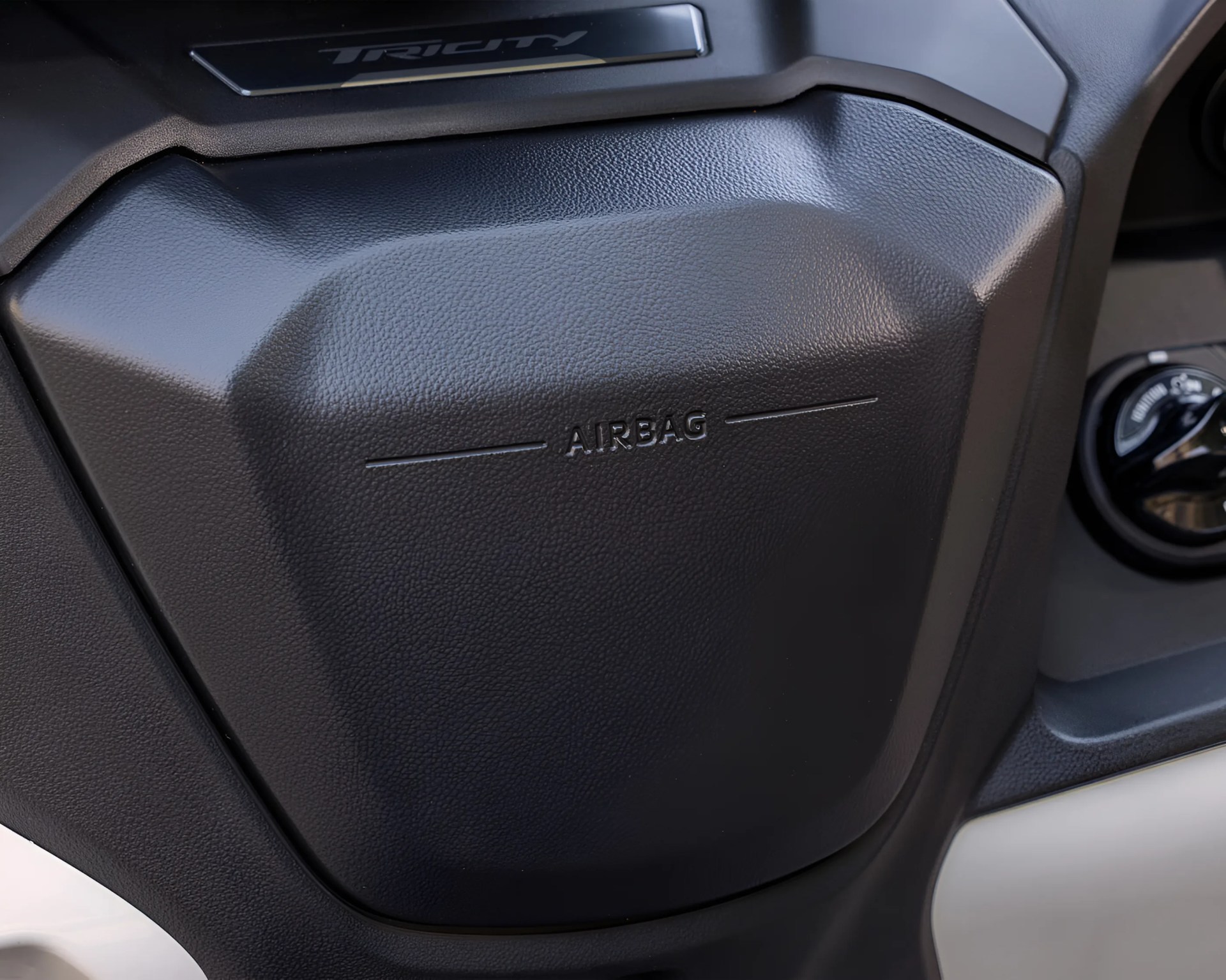 Black textured plastic airbag cover on a vehicle dashboard with "TRICITY" branding above.