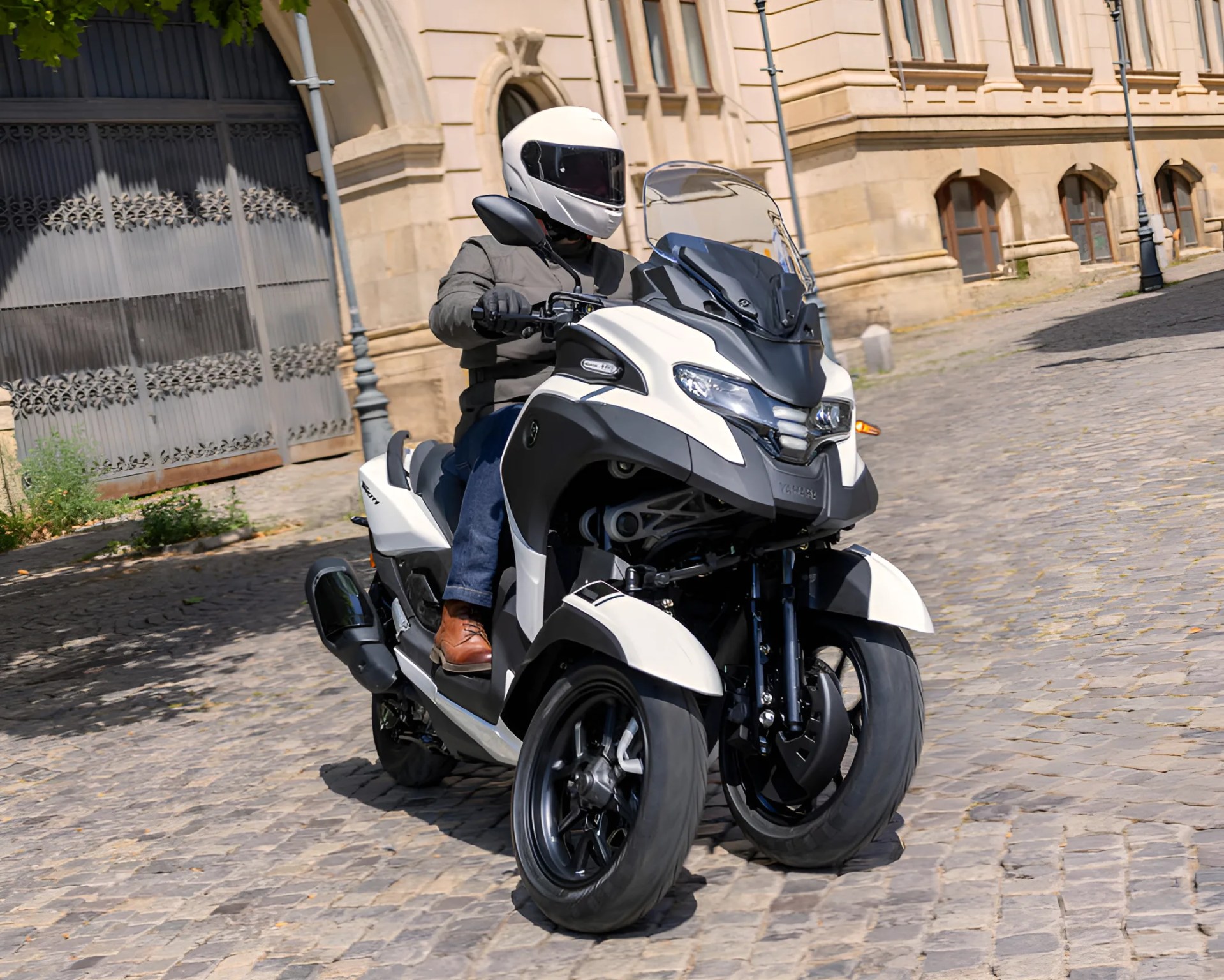 White three-wheeled scooter with black accents ridden on a cobblestone street.