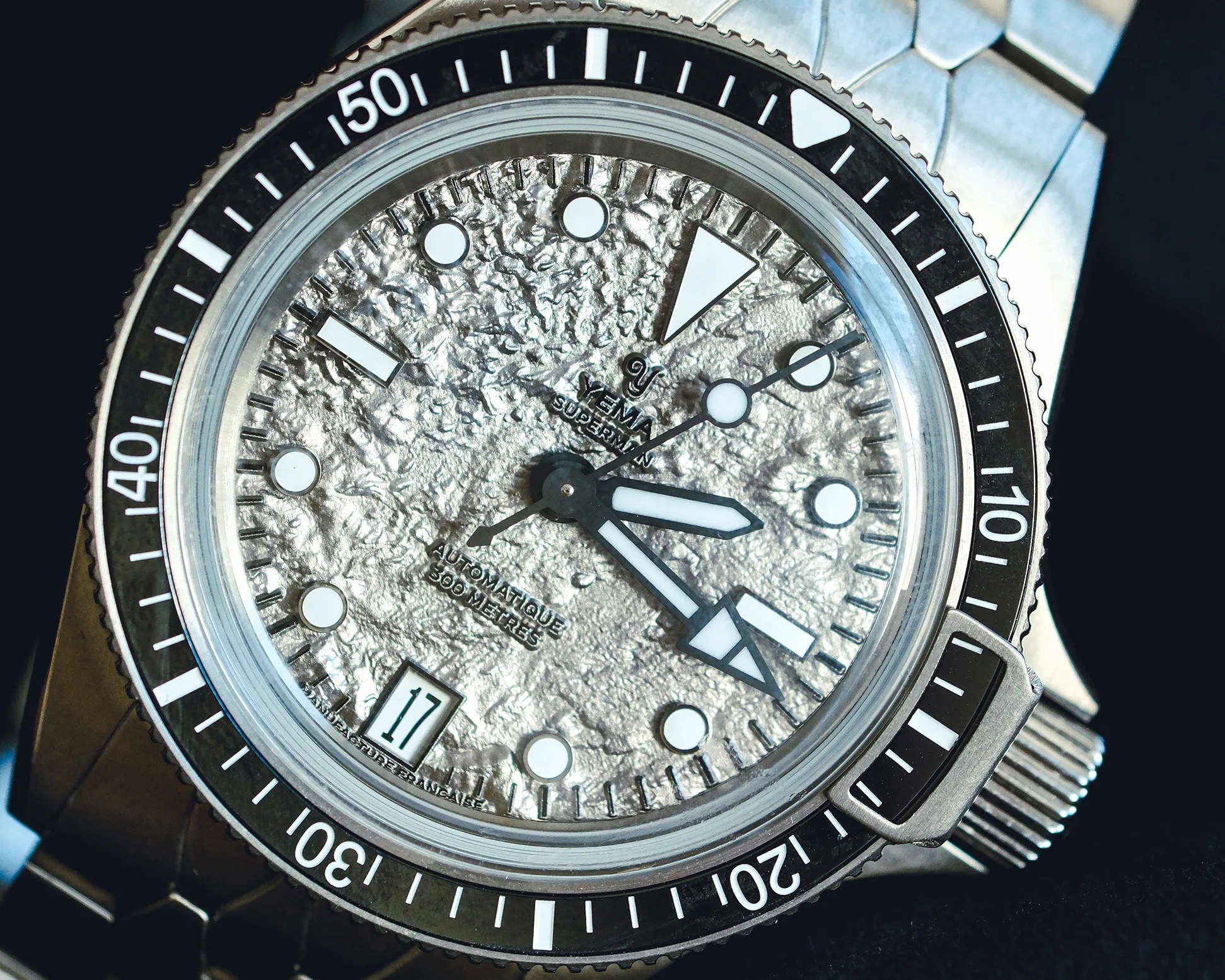 Close-up of a Yema Superman dive watch with a textured silver dial, black bezel, and stainless steel bracelet.