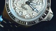 Close-up of a silver textured dial watch with black and white bezel, luminous hands, date window showing 17, and metal bracelet.