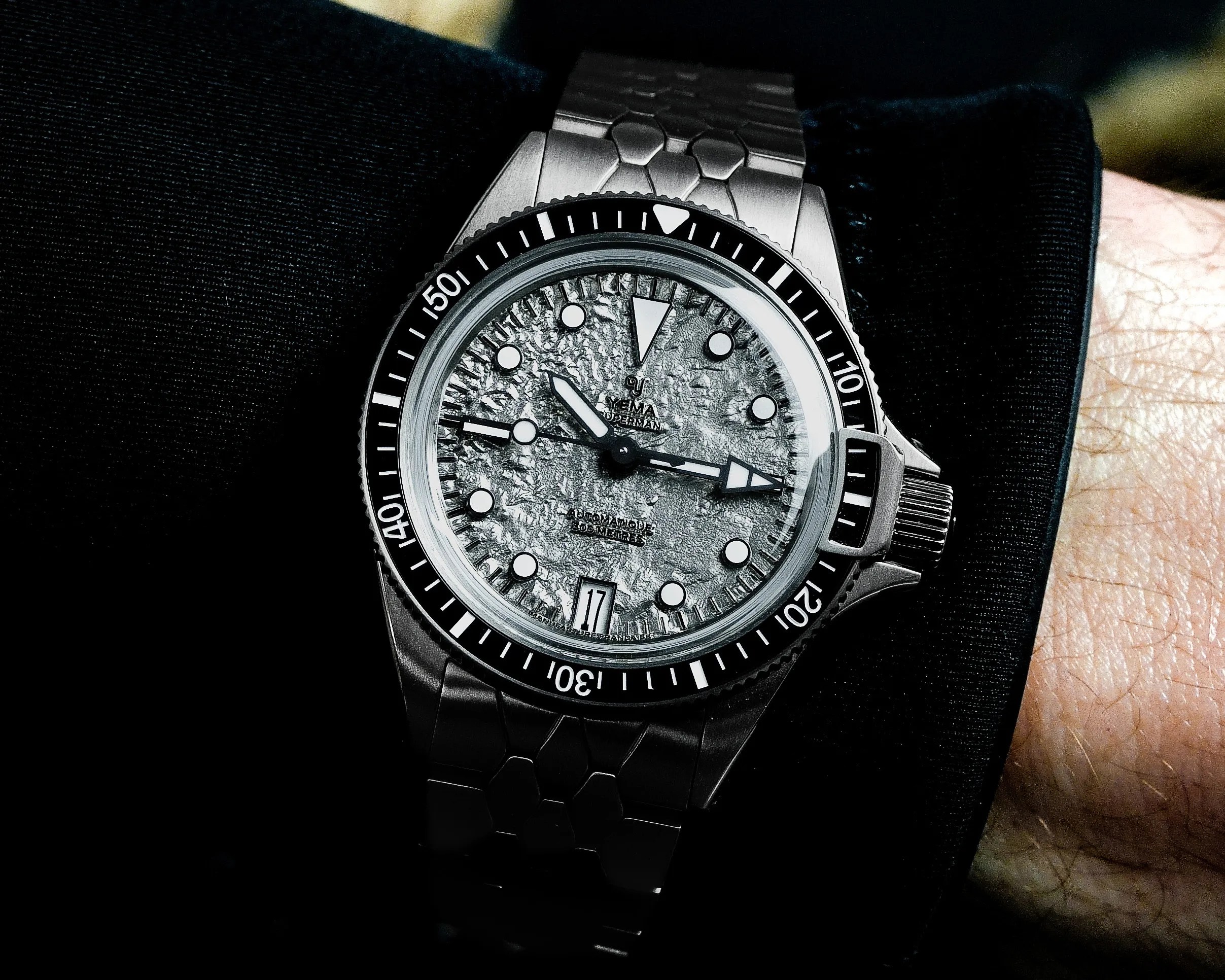 Silver stainless steel wristwatch with textured dial, black bezel, and date display worn on a wrist.