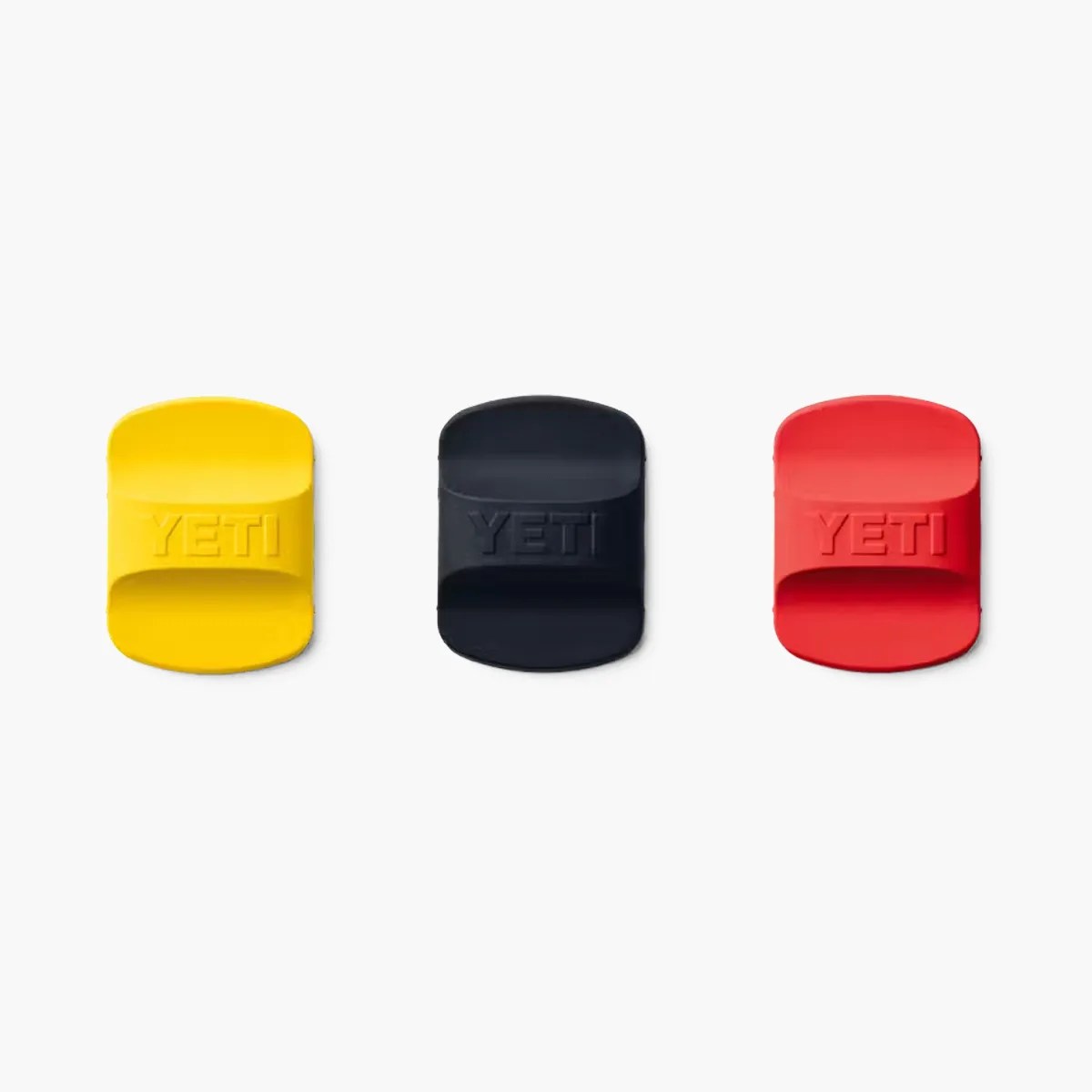 Three rectangular YETI branded silicone clips in yellow, black, and red on a white background.