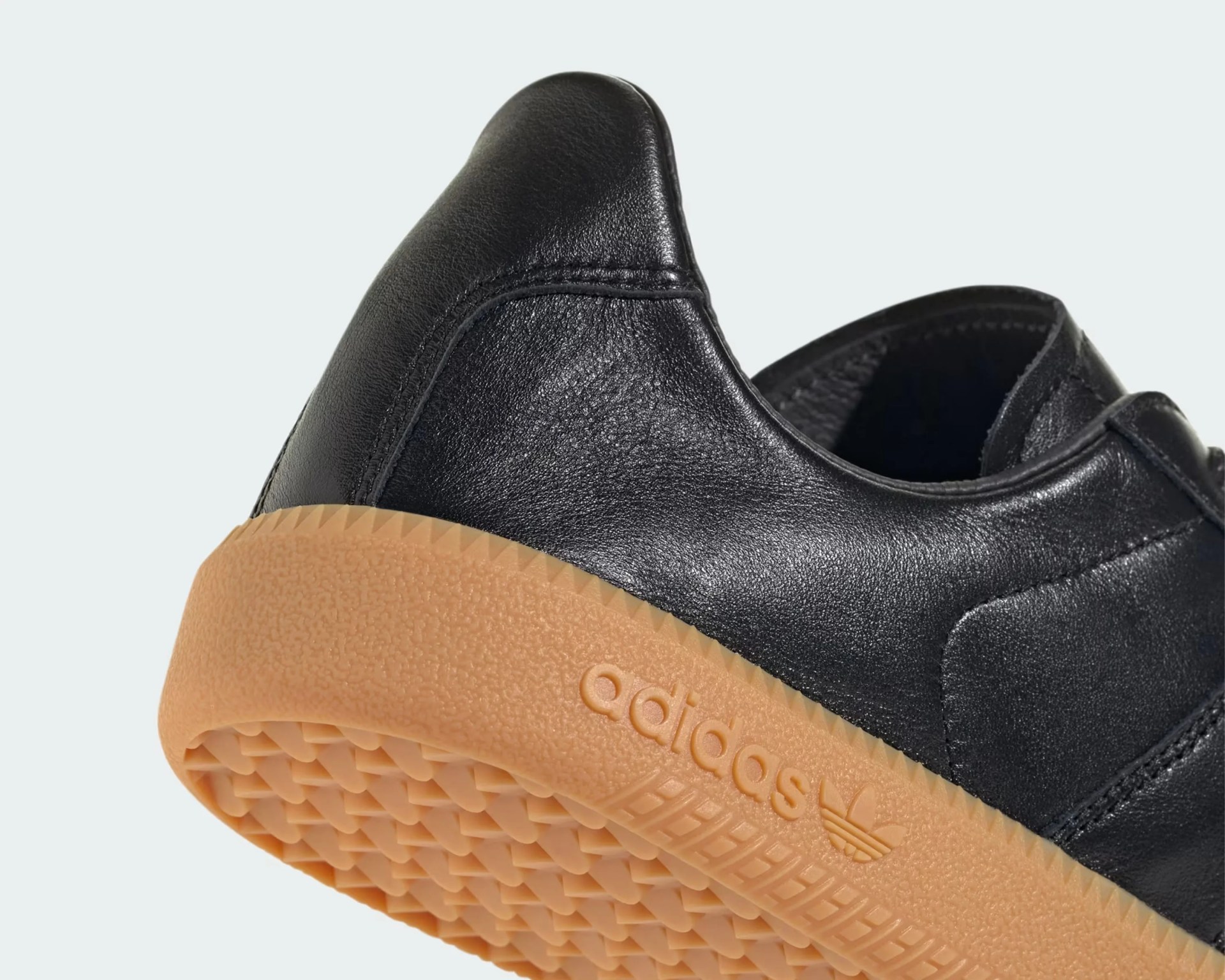Close-up of black leather Adidas shoe with textured gum sole and Adidas logo embossed on the side.