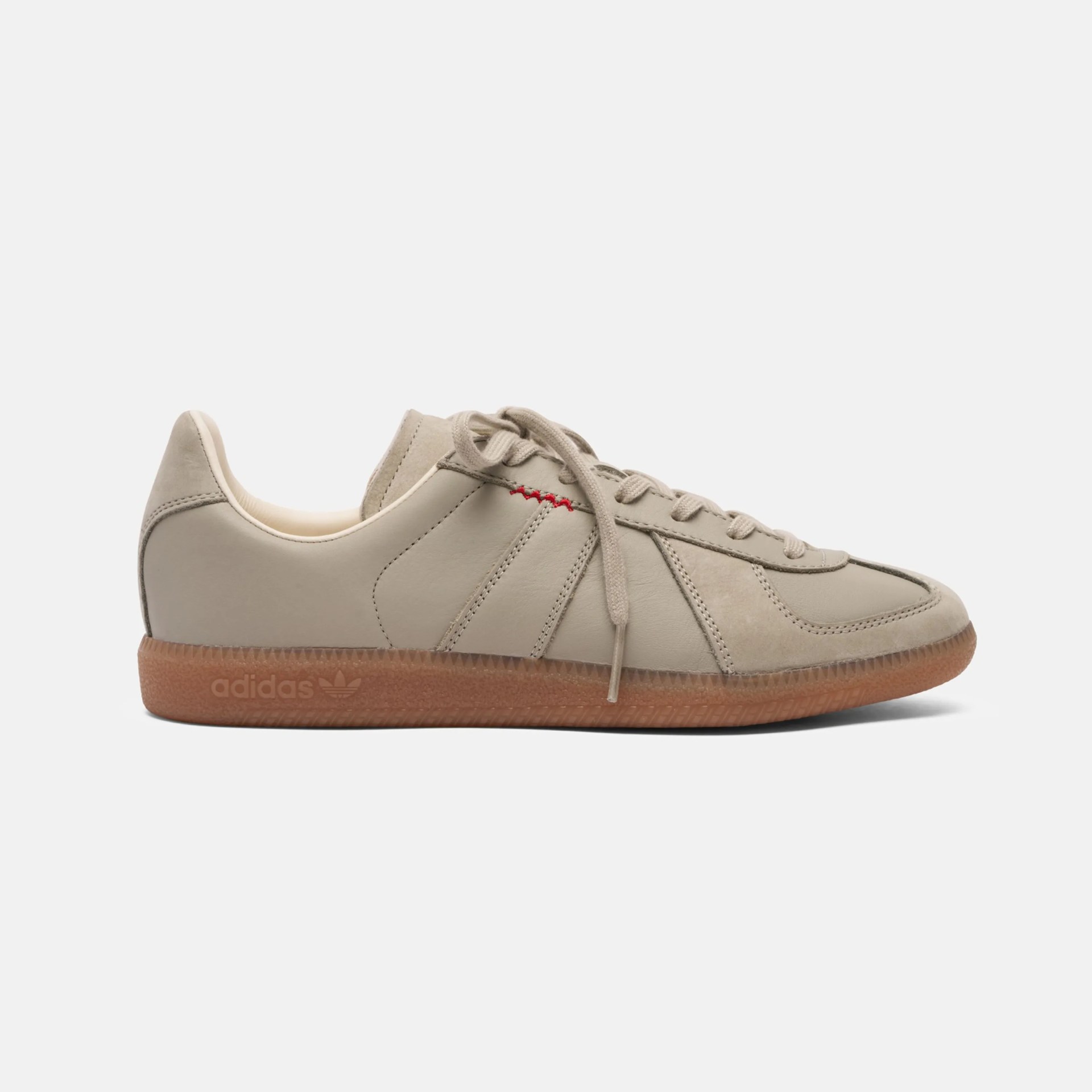 Beige leather Adidas sneaker with gum sole and red stitching detail on side.