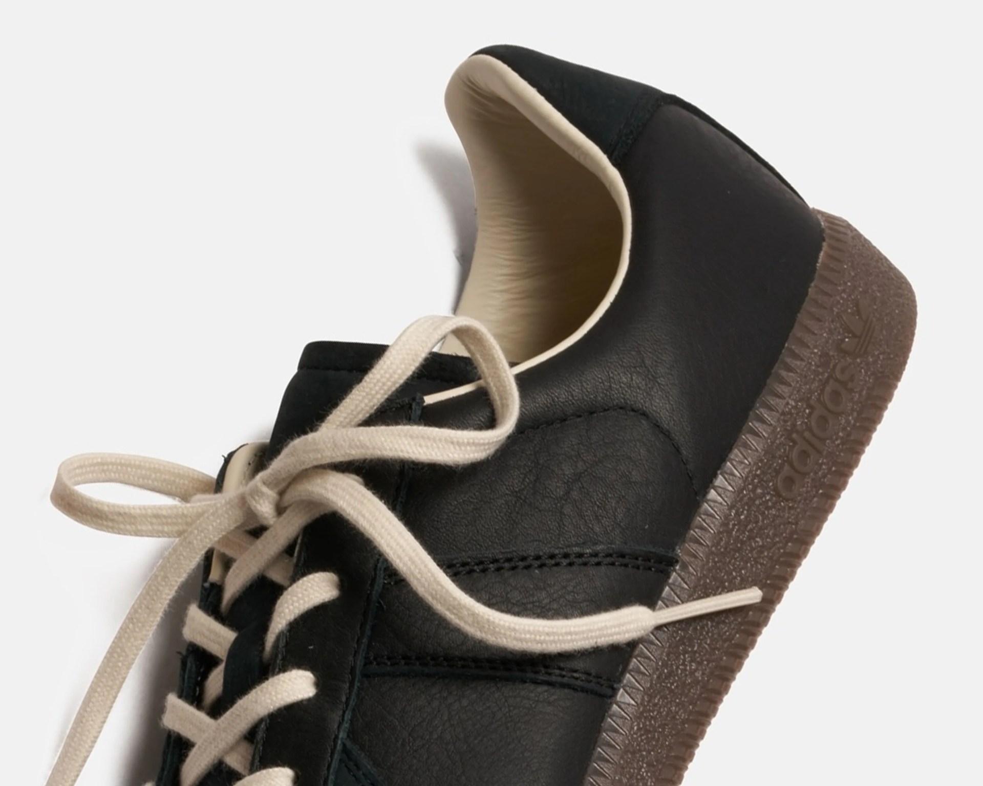 Black leather Adidas sneaker with beige laces and brown textured sole.