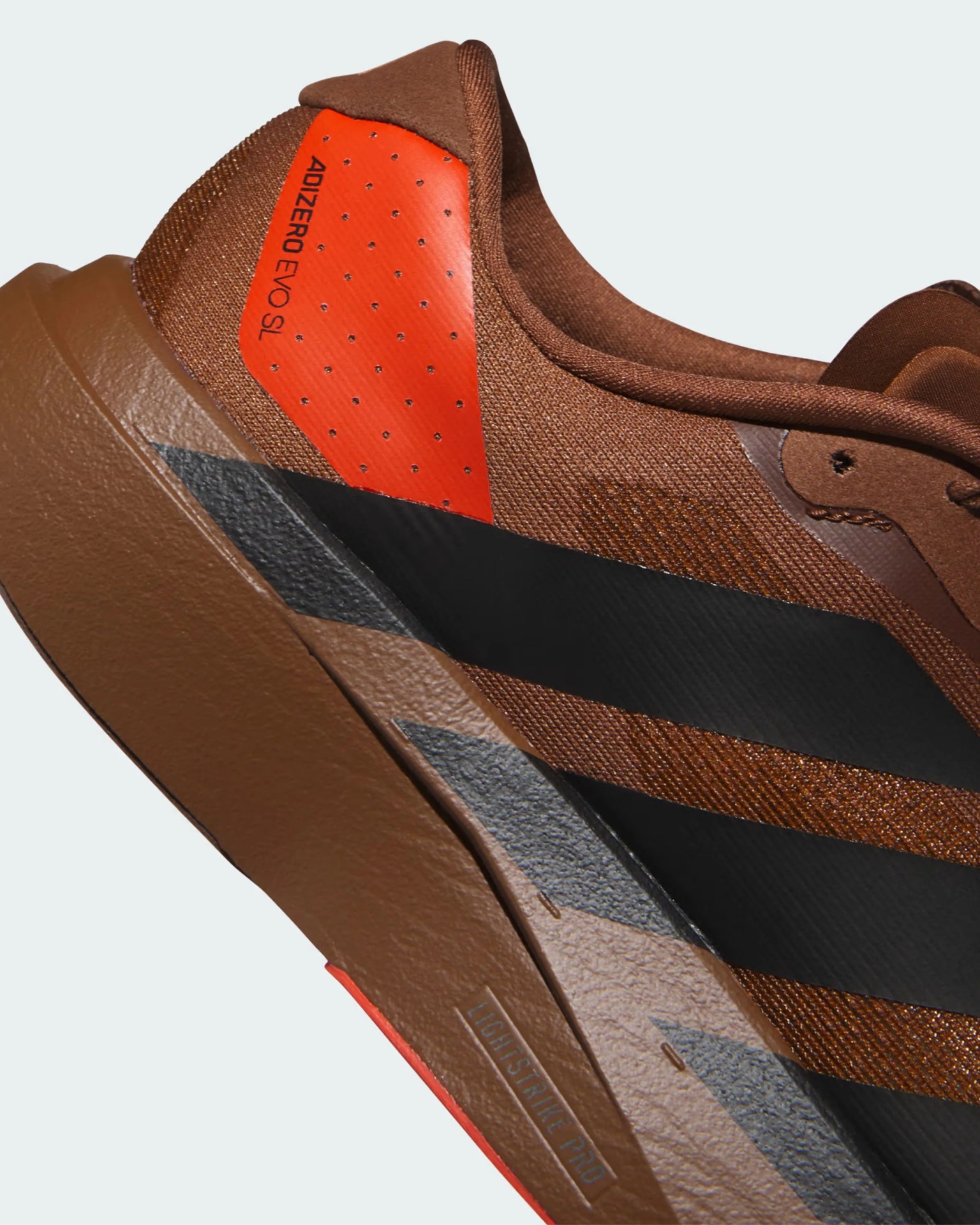 Close-up of a brown Adidas Adizero SL running shoe with black stripes and orange heel detail.