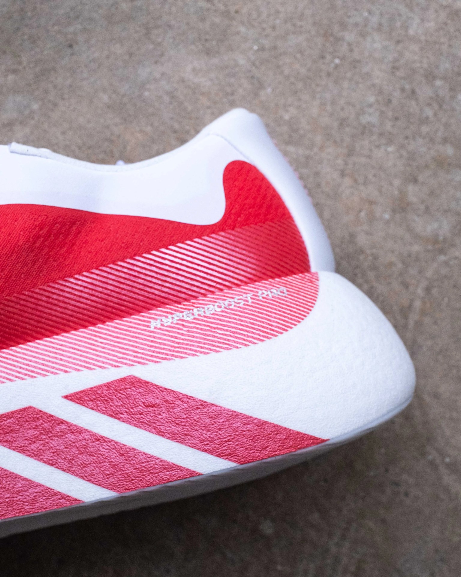 Close-up of a white and red athletic shoe heel with textured sole and diagonal stripes on a concrete surface.
