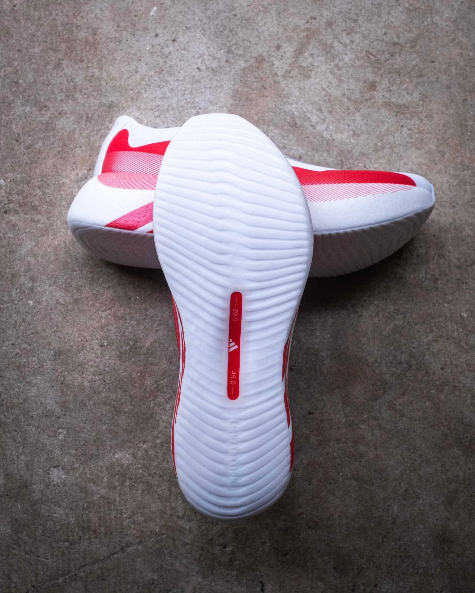 Pair of white and red athletic shoes with textured white soles and Adidas logo on the sole.