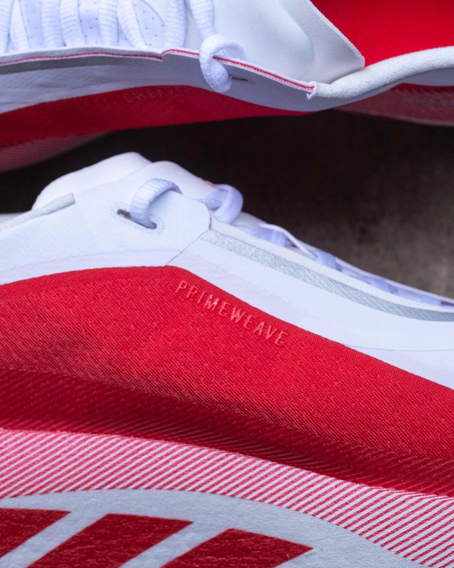 Close-up of red and white sneakers with "PRIMEWEAVE" text on the red fabric near the laces.