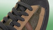 Close-up of a sneaker with black laces, brown suede panels, dark brown leather stripe, and textured black rubber sole.