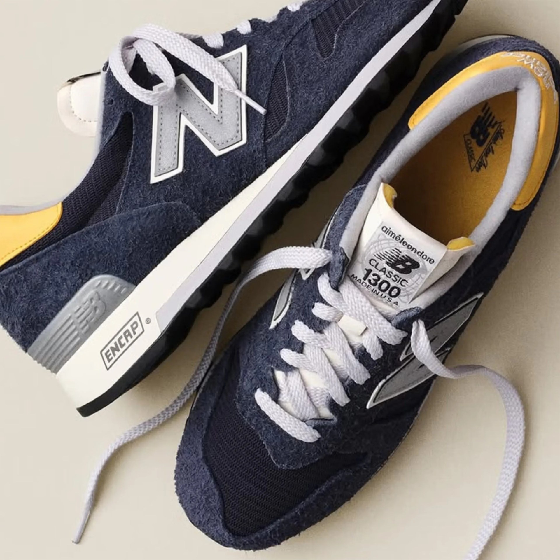 Pair of navy blue New Balance Classic 1300 sneakers with white laces, gray accents, and yellow inner lining.