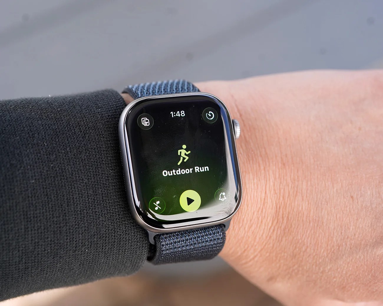 Smartwatch with a blue woven band displaying an "Outdoor Run" workout screen on a wrist.